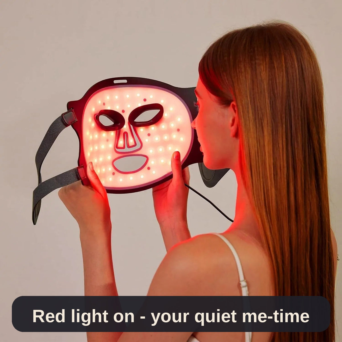 Woman holding the black LED face mask while its red lights glow - a quiet few minutes of me-time in her evening routine.