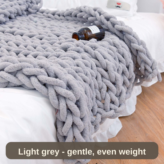 Knitted Weighted Blanket in light grey draped over a bed - chunky hand-knit loops with a gentle, even weight.